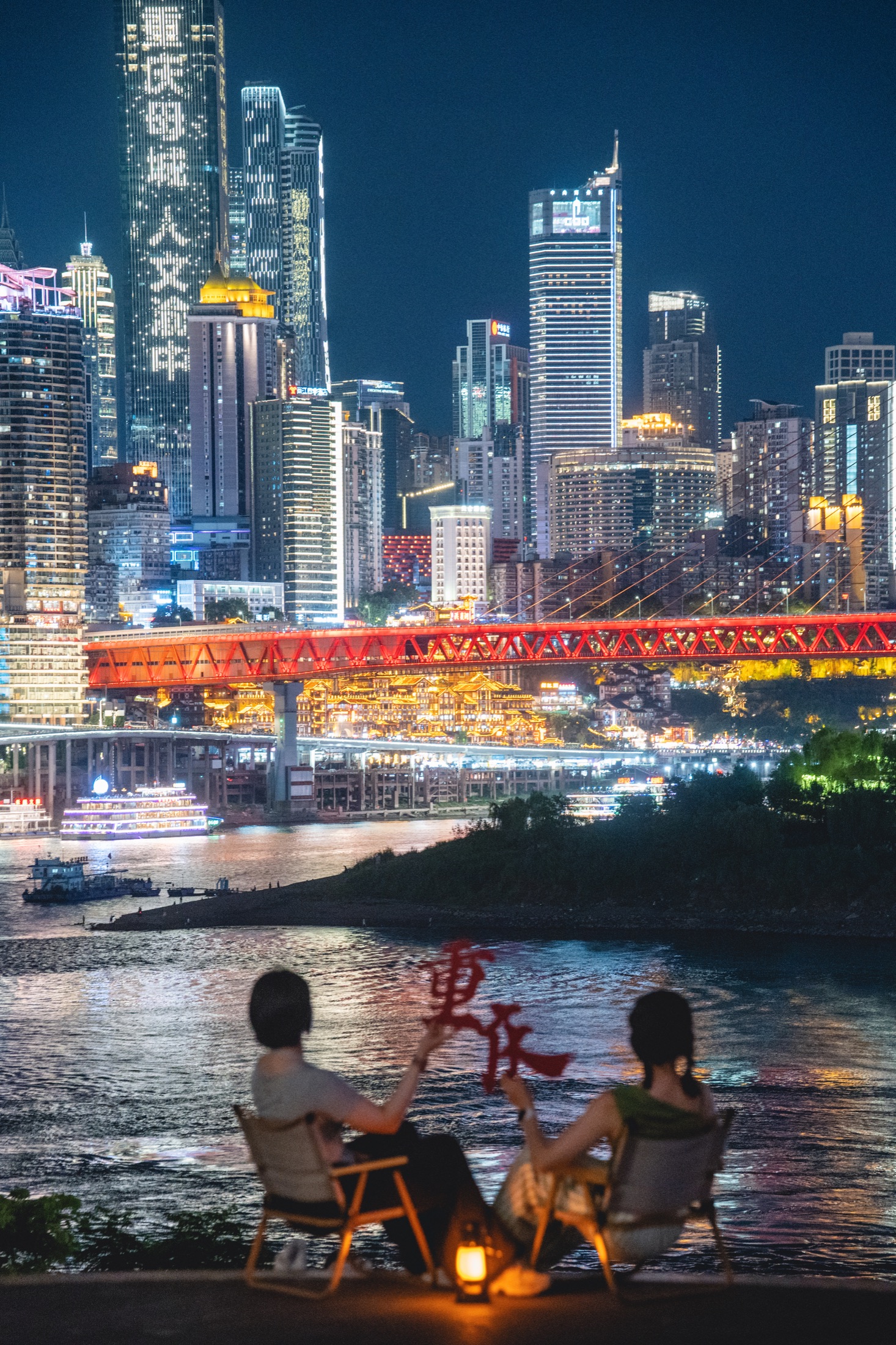 两位旅行者坐在江边欣赏重庆夜景
